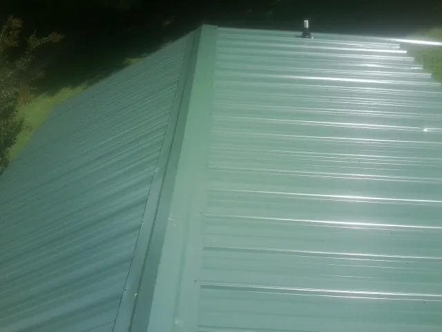 New green metal panels meeting at the ridge of a roof — Flat Roof Repair work by our crew in Cushing