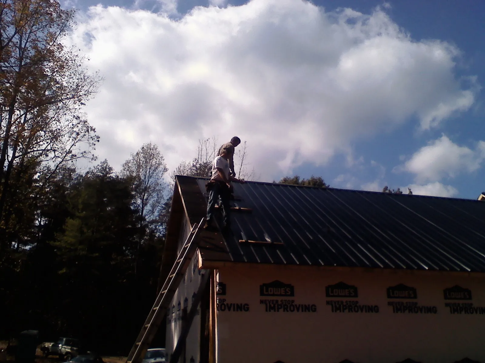 Roofer fastening dark metal panels high against a cloudy sky, from a Roof Inspection job in Cushing
