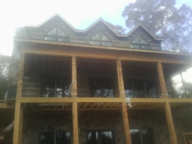 Dormers and porch framing on a large log home under construction — Roof Coating work by our crew in Cushing